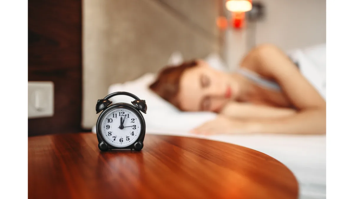 Schlafende Frau im Bett, im Vordergrund ein Wecker